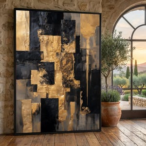Pode incluir: Obra de arte abstrata com moldura preta. A obra apresenta um design texturizado com formas retangulares douradas e pretas. A pintura é exibida em um piso de madeira, com vista para um jardim através de uma grande janela.