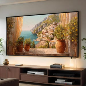 May include: A framed landscape painting depicts a coastal Italian town with colorful buildings, a beach, and the sea. The artwork features potted plants with yellow fruit and a warm color palette. The painting is displayed above a brown wooden cabinet.