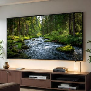 May include: A large, rectangular television displaying a scenic river flowing through a lush green forest. The TV is mounted on a light-colored wall above a dark brown wooden entertainment center. A small lamp and decorative items are on the center.