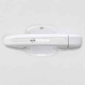Może przedstawiać: Biała klamka samochodowa Nissan z dopasowaną białą osłoną miseczki. Klamka posiada logo Nissan oraz nadrukowany na biało napis NISSAN. Osłona miseczki również prezentuje logo Nissan oraz biały napis NISSAN na swojej powierzchni.