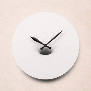 May include: A white wall clock with black hands and a unique design. The clock face has a subtle grid pattern that appears to recede into a central black hole-like feature. The hands are black and pointed.