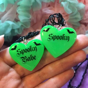 May include: Two green heart-shaped necklaces with black chains. The hearts have black bats and the text "Spooky" and "Spooky Babe" printed on them.