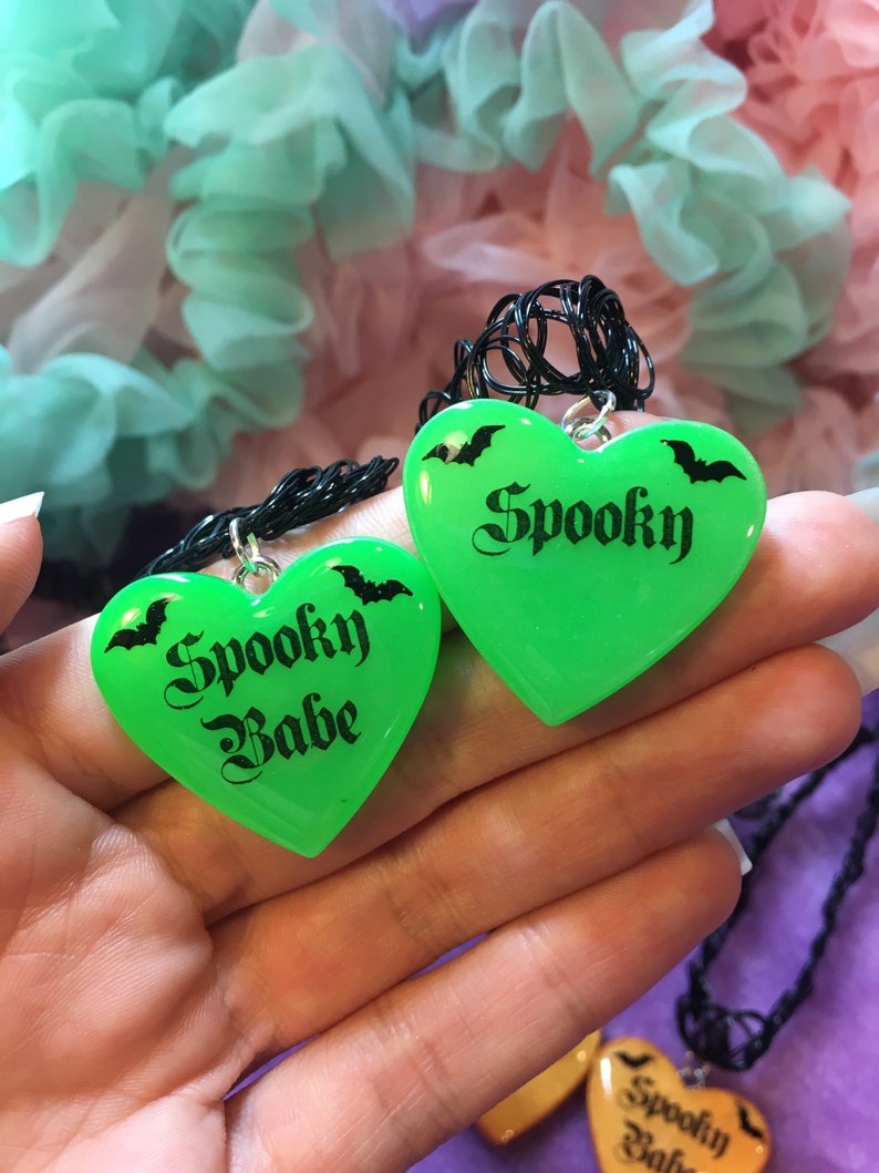 May include: Two green heart-shaped necklaces with black chains. The hearts have black bats and the text "Spooky" and "Spooky Babe" printed on them.