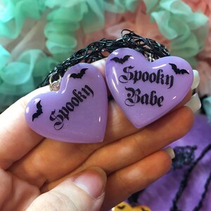 May include: Two purple heart-shaped charms with black bats and the text "Spooky" and "Spooky Babe" on a black choker necklace.