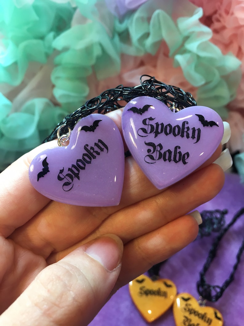 May include: Two purple heart-shaped charms with black bats and the text "Spooky" and "Spooky Babe" on a black choker necklace.