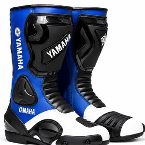 Puede incluir: Un par de botas de moto Yamaha azules, negras y blancas. Las botas muestran el logotipo de Yamaha y tienen un diseño alto. Están diseñadas para la protección y tienen secciones reforzadas.