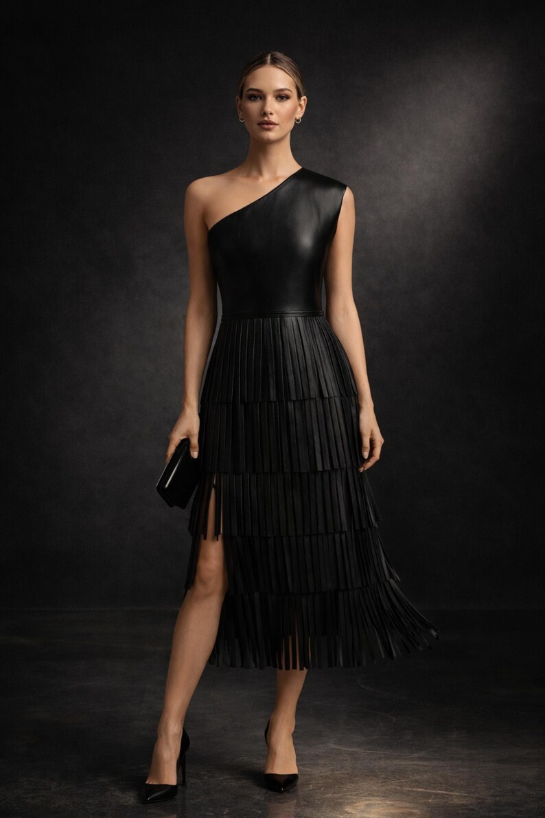 Black one shoulder leather dress with layered fringe midi skirt worn by model in dark luxury studio setting, elegant asymmetrical evening party outfit full body view