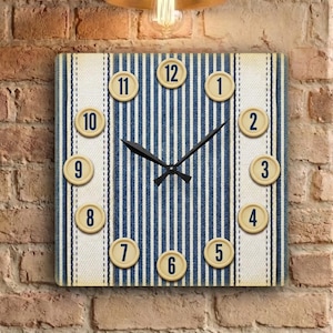 May include: Square wall clock with a blue and white striped face, featuring beige number markers. The clock is mounted on a brick wall, with a vintage-style light fixture above. A poster for "The Vinyl Grind" is visible.