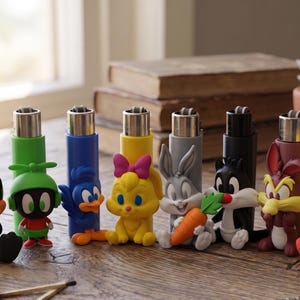 May include: A collection of eight refillable lighters, each featuring a three-dimensional Looney Tunes character figure attached to the front. The characters include Daffy Duck, Marvin the Martian, Road Runner, Lola Bunny, Bugs Bunny, Sylvester, Wile E. Coyote, and Tweety Bird, all rendered in vibrant colours.