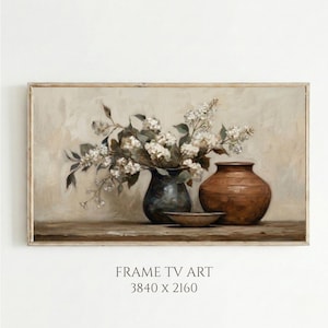 May include: A framed digital art print featuring a still life composition. A dark blue vase holds white flowers with green leaves. A brown vase and a small bowl sit beside the vase. The text "FRAME TV ART 3840 X 2160" is at the bottom.