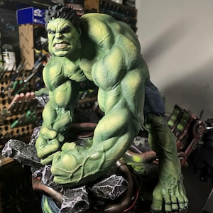 Può includere: Una dettagliata statuetta verde di Hulk in una posa accovacciata e aggressiva con i pugni chiusi. Il personaggio presenta una marcata definizione muscolare, capelli scuri ed è posizionato su una base di detriti scuri e frastagliati.