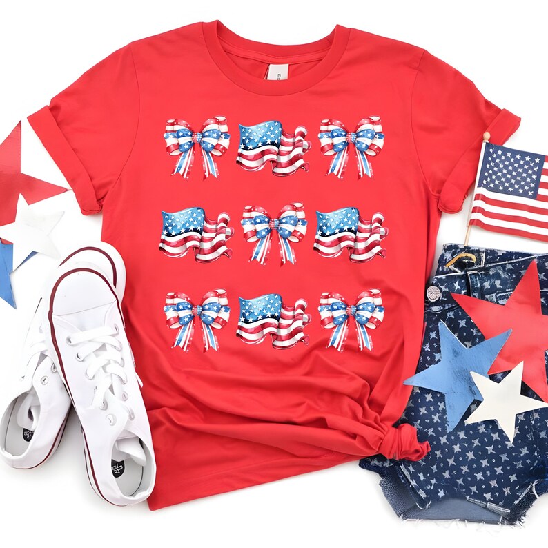 May include: A red t-shirt featuring a patriotic design with bows and American flags. The shirt is paired with white sneakers and denim shorts with star cutouts. An American flag is also present.