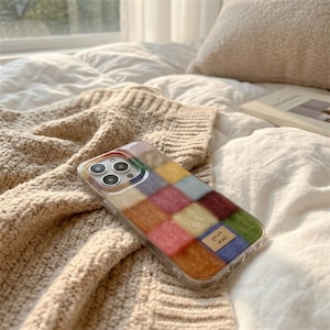 Op de afbeelding: Een transparante telefoonhoes met een kleurrijk patchwork-ontwerp. De hoes heeft een raster van vierkanten in verschillende kleuren, waaronder rood, geel, groen en blauw. Een klein label met tekst is zichtbaar rechtsonder.