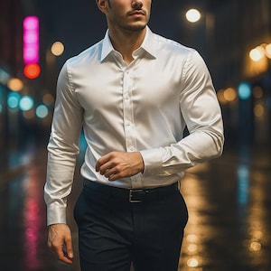 Puede incluir: Una camisa blanca de manga larga con cuello clásico. Se combina con pantalones azul marino oscuro y un cinturón negro. La tela tiene un brillo sutil, lo que sugiere satén o seda. La imagen se toma al aire libre por la noche.