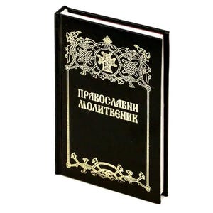 Puede incluir: Un libro negro con diseños y texto dorados. La portada presenta un borde decorativo y un emblema central. El texto de la portada dice "Православни молитвеник". El libro tiene un borde blanco.