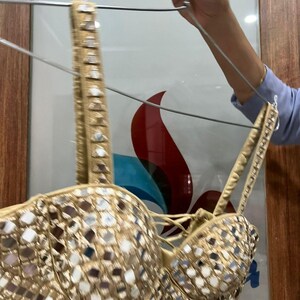 May include: A gold-colored bustier top with a mirrored design. The top has adjustable straps and a lace-up front. The bustier is hanging on a hanger.