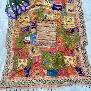 May include: A colorful textile with a patchwork design featuring paisley and floral patterns in shades of orange, green, and purple. The fabric is adorned with small mirrors and a decorative border with tassels. A matching top is also included.