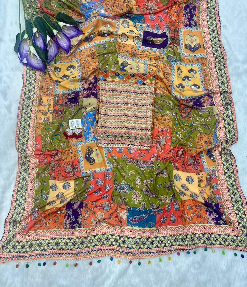 May include: A colorful textile with a patchwork design featuring paisley and floral patterns in shades of orange, green, and purple. The fabric is adorned with small mirrors and a decorative border with tassels. A matching top is also included.