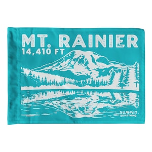 May include: A turquoise flag with a white graphic of Mount Rainier, a mountain range, and a lake. The text "MT. RAINIER 14,410 FT" is at the top. The text "SUMMIT. SOMETHING" is at the bottom.