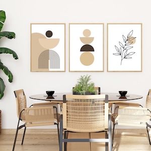 May include: Three framed abstract art prints with geometric shapes and a botanical design in neutral tones. The prints are displayed above a dining table with woven chairs and a plant centerpiece, creating a modern interior design.