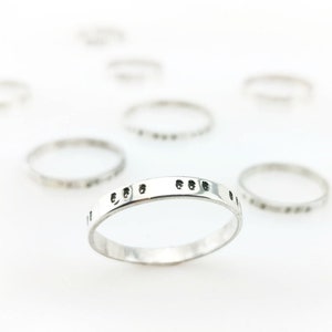 May include: A close-up of a silver ring with a textured band. The ring is on a white background.