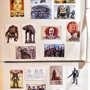 May include: A collection of magnets on a white refrigerator. The magnets feature illustrations of characters from popular movies and TV shows, including Pennywise the Dancing Clown, the Predator, the Alien, and the Terminator. There are also magnets with illustrations of a creature from the movie "Gremlins", a Star Wars AT-ST walker, and a group of clowns. The magnets are all different sizes and shapes, and they are arranged in a random pattern on the refrigerator.