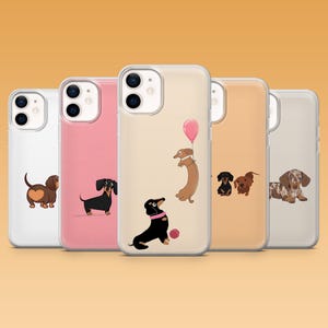 Op de afbeelding: Een verzameling telefoonhoesjes met illustraties van teckel honden. De hoesjes tonen verschillende ontwerpen, waaronder een bruine hond met een hart, een zwarte hond en een teckel met een roze ballon. De hoesjes zijn in verschillende kleuren.