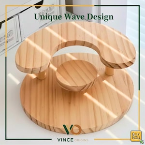 May include: A wooden display stand with a unique wave design. The stand is made of light-coloured wood and features a circular base, a central platform, and a curved top section. The text "Unique Wave Design" is visible.