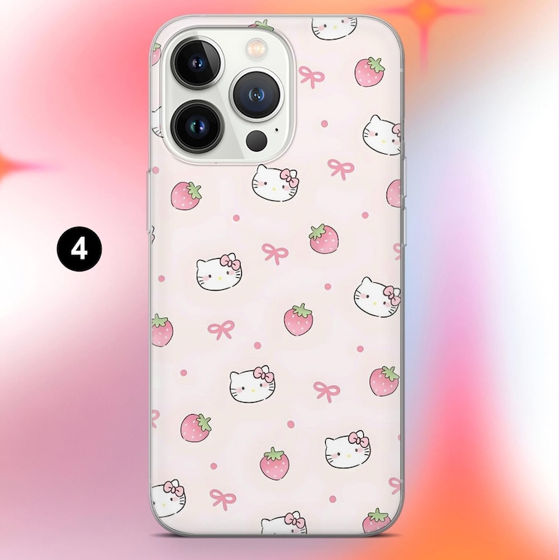 May include: A clear phone case featuring a repeating pattern of cartoon cat faces with bows, strawberries, and pink bows on a light pink background. The phone case has a clear border and a camera cutout.