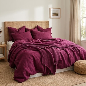 Puede incluir: Una cama vestida con ropa de cama de color magenta intenso, que incluye una funda nórdica, cuatro fundas de almohada a juego y una manta con textura de tejido de gofre. La cama tiene un cabecero de ratán trenzado contra una pared blanca.