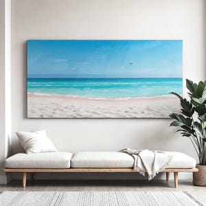 以下が含まれることがあります： ビーチの風景を描いた、大きな長方形のキャンバス絵画。明るい青い空、ターコイズブルーの水、白い砂浜、小さな鳥が描かれています。絵画は、白いクッションと装飾的なスローが付いた、明るい色の木製ベンチの上に展示されています。