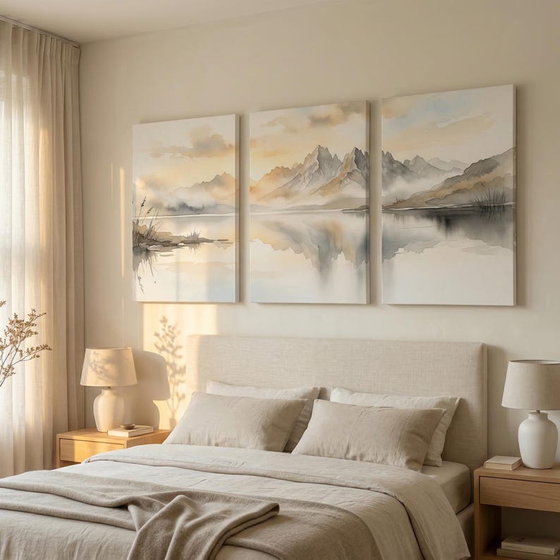 May include: A triptych wall art set featuring a watercolor landscape of misty mountains reflected in a calm lake. The artwork uses a soft palette of beige, grey, and muted gold tones, depicting jagged peaks, low clouds, and shoreline reeds.