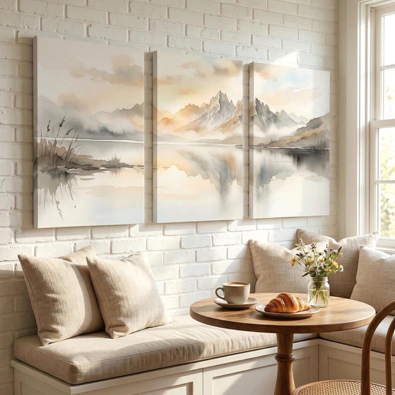 May include: A triptych wall art set featuring a watercolor landscape of misty mountains reflected in a calm lake. The artwork uses a soft palette of beige, gray, and white tones, depicting jagged peaks, distant clouds, and shoreline reeds.