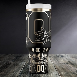 May include: Black tumbler with gold detailing and a white lid. The tumbler features the Ohio State logo, the letter "O", floral designs, and the text "O-H I-O" and "OHIO STATE 00".