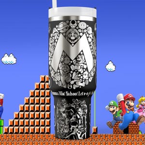 May include: A black and silver insulated tumbler featuring a large silver "M" design filled with various Mario characters. The tumbler has a white lid and straw. The background depicts a classic Super Mario Bros. scene with characters and pixelated elements.