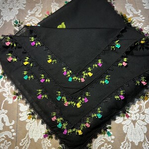 Peut inclure: Foulard carré noir avec broderie florale colorée sur les bords. La broderie présente des fleurs roses, jaunes et vertes. Le foulard est plié, mettant en valeur le design et le savoir-faire.