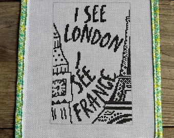 May include: A framed needlepoint with the text "I SEE LONDON I SEE FRANCE" in black. The artwork features illustrations of the Eiffel Tower and a building, framed with a green and yellow floral fabric.