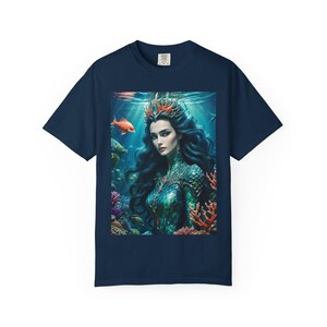 Könnte beinhalten: Marineblaues T-Shirt mit einer lebendigen Illustration einer Meerjungfrau in einer Unterwasserszene. Das Kunstwerk zeigt eine Meerjungfrau mit langen, dunklen Haaren, einer Krone und einem schuppenartigen Oberteil, umgeben von Korallen, Fischen und Wasserpflanzen.