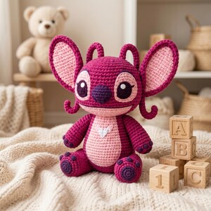 May include: A crochet plush toy featuring a dark magenta body with a light pink belly and inner ears. The character has large pointed ears, dark purple eyes, a dark purple nose, and a small white heart-shaped detail on the chest area.