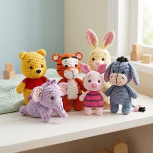 May include: A collection of six crocheted stuffed animal figures including a yellow bear in a red shirt, an orange and black striped tiger, a light purple elephant, a pink piglet, a yellow rabbit, and a blue donkey with a black tail tuft.