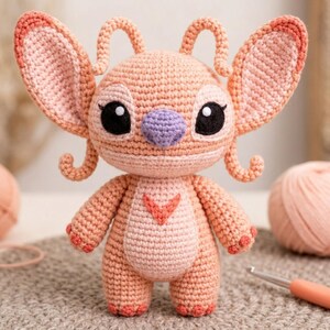 May include: A peach-colored crochet doll featuring large pointed ears, two curled antennae, and a light pink belly patch with a V-shaped detail. The doll has large black eyes with white highlights, a lavender nose, and small pink paw pads on its feet.