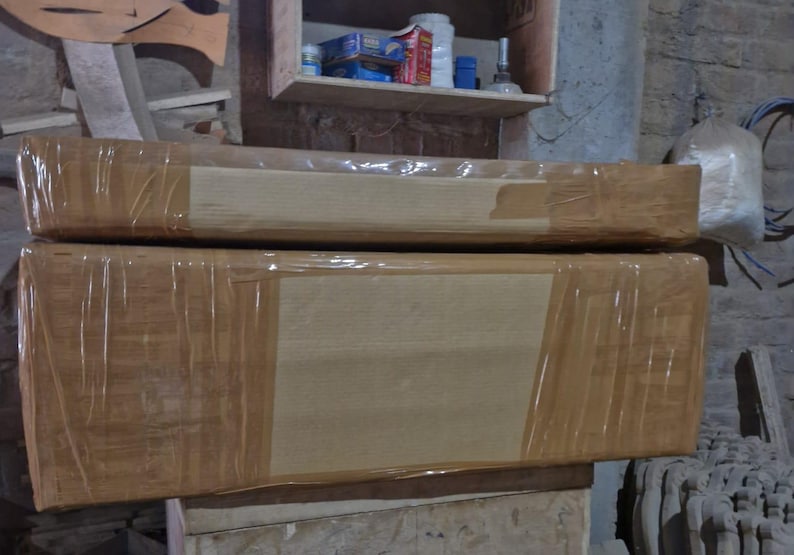 May include: Two rectangular wooden objects stacked vertically, each wrapped in clear plastic film and secured with wide tan adhesive tape. The surfaces are smooth and light brown, showing the natural grain of the wood beneath the protective packaging.