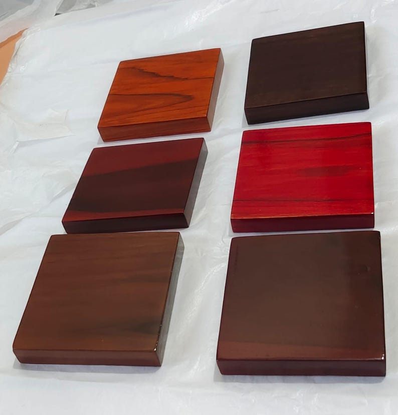 May include: Six square wooden blocks arranged in two columns of three. Each block features a distinct wood grain pattern and a polished finish, displaying a variety of warm tones including light orange, deep red, and dark brown wood shades.