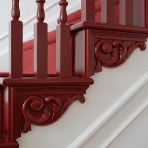 May include: Close-up of a staircase with a red carpet and dark red wooden banisters. The banisters have decorative carved details and are set against a white wall with molding.