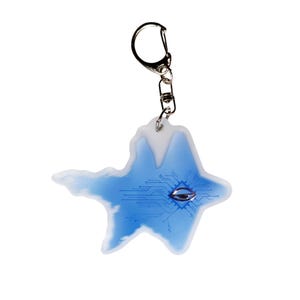 May include: A unique keychain featuring a blue and white abstract design with a circuit board pattern and a silver-colored eye-shaped detail. The keychain is attached to a silver-colored metal ring.