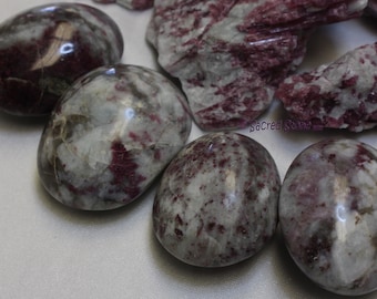 May include: Close-up of several polished stones with a mix of colors. The stones are primarily gray and white, with streaks and spots of deep red. Some stones are egg-shaped, while others are rougher.