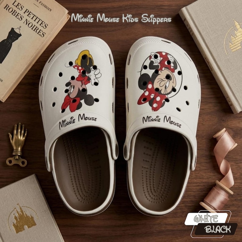 K&ouml;nnte beinhalten: Paar wei&szlig;e Minnie Mouse Kinderslipper. Jeder Slipper zeigt eine andere Minnie Mouse Grafik in Rot, Schwarz und Gelb. Die Slipper haben braune Sohlen und der Text "Minnie Mouse" ist auf der Vorderseite aufgedruckt.