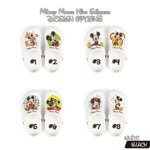 K&ouml;nnte beinhalten: Wei&szlig;e Mickey Mouse Kinderslipper mit verschiedenen Designs, darunter Mickey Mouse in verschiedenen Posen. Das Bild zeigt acht Paar Hausschuhe, jedes mit einem einzigartigen Grafikdesign und einer Nummer von 1 bis 8.