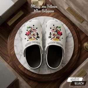 Op de afbeelding: Witte Disney Friends kinderslippers met een zwarte zool. De slippers hebben een kleurrijke afbeelding van Mickey Mouse, Minnie Mouse, Donald Duck en andere Disney-figuren. De tekst "Mickey and Friends Kids Slippers" en "Disney Friends" is gedrukt.