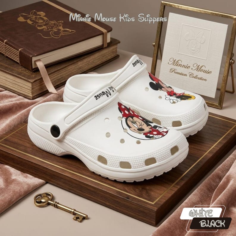 K&ouml;nnte beinhalten: Wei&szlig;e Minnie Mouse Kinderclogs mit einem Minnie Mouse Cartoon-Motiv. Die Clogs haben einen Riemen und werden auf einem Holztablett pr&auml;sentiert. Der Text "Minnie Mouse Kids Slippers" ist sichtbar.